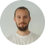 Smiling person with beard and bun, wearing white shirt.